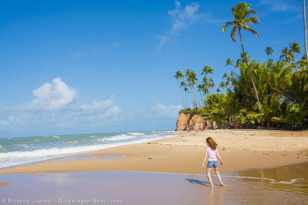 Imagem de uma menina molhando os pés nas águas cristalinas da Praia Barra do Cahy.